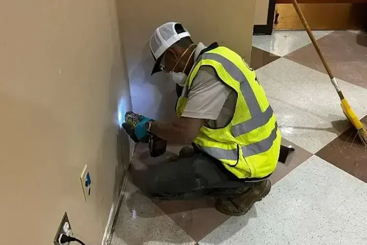 A technician in a safety vest checking a wet wall with a moisture meter