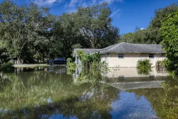 A single-story home surrounded by standing floodwater under tall trees