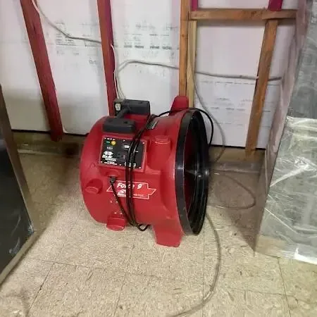 Bellflower water damage: red air mover and plastic by an opened wall