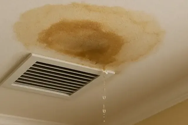 A ceiling stain and dripping water beside an AC supply vent from a clogged condensate drain