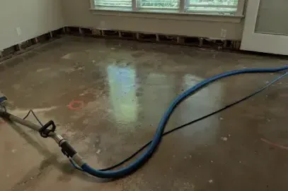 Extraction hose clearing water from a wet concrete floor inside a home